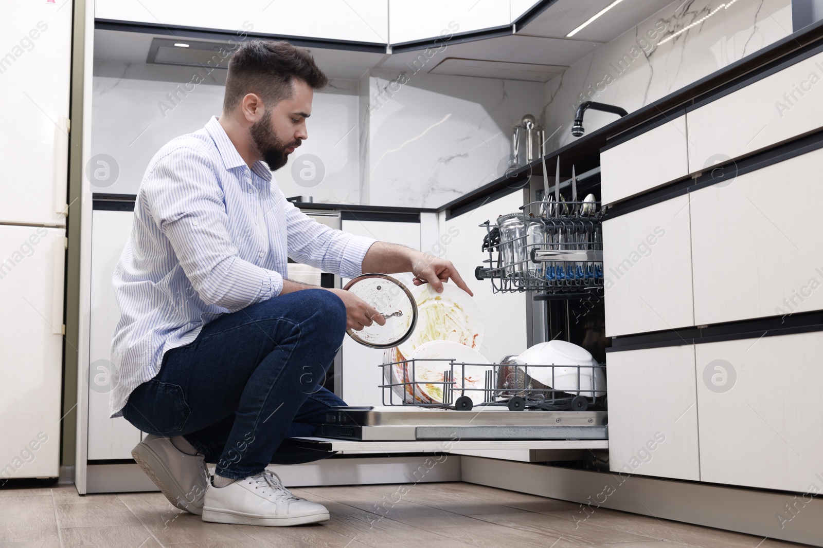 Photo of Man loading dishwasher with dirty plates indoors