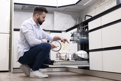 Man loading dishwasher with dirty plates indoors