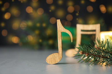 Photo of Wooden music note and fir branches on light grey table against blurred Christmas lights