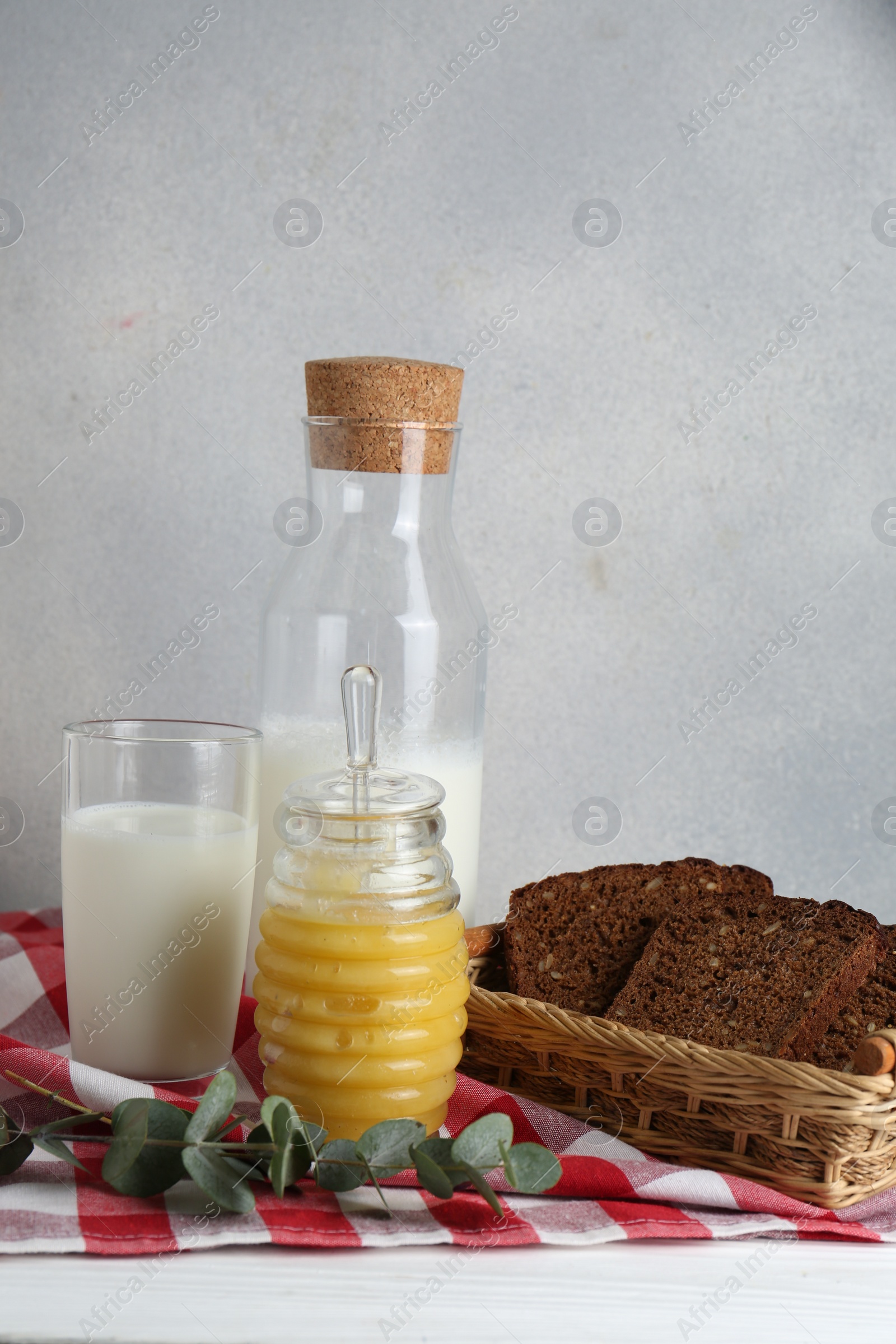 Photo of Jar with tasty honey, milk and bread on white wooden table