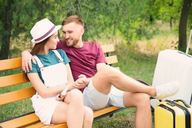 Photo of Young couple with suitcases packed for summer journey sitting on bench
