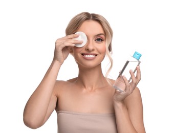 Smiling woman removing makeup with cotton pad and holding bottle on white background