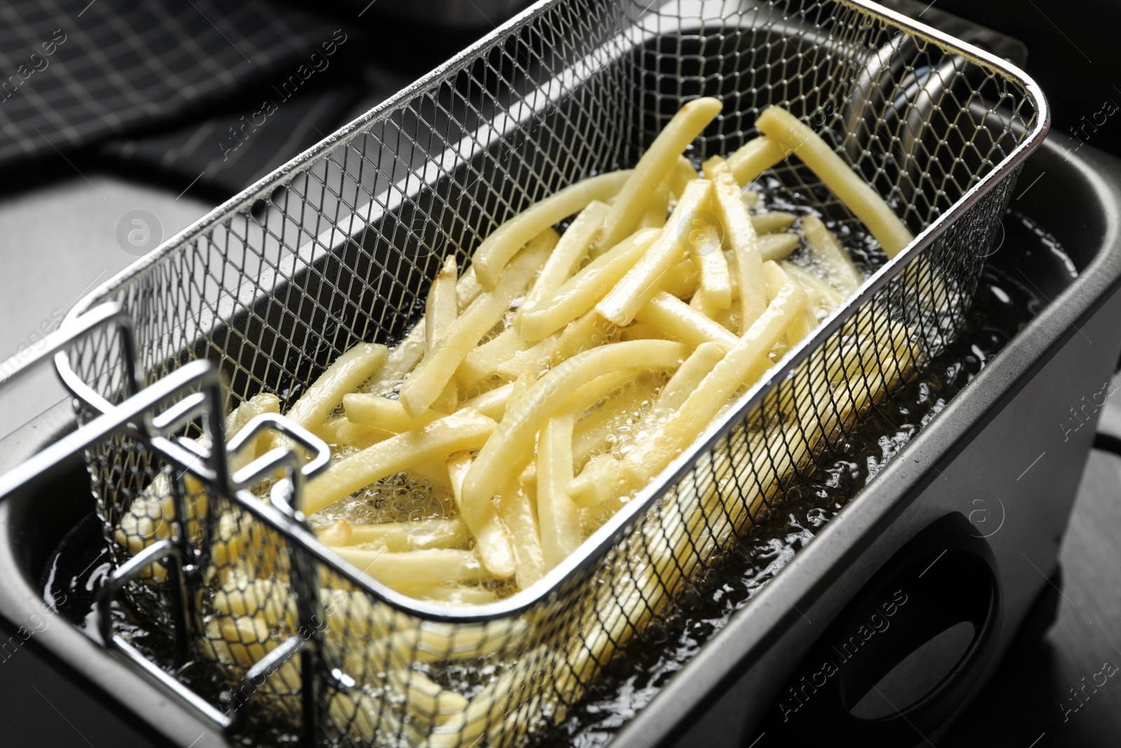 Photo of Cooking delicious french fries in hot oil, closeup