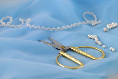 Photo of Pair of scissors and white beads on light blue fabric, closeup