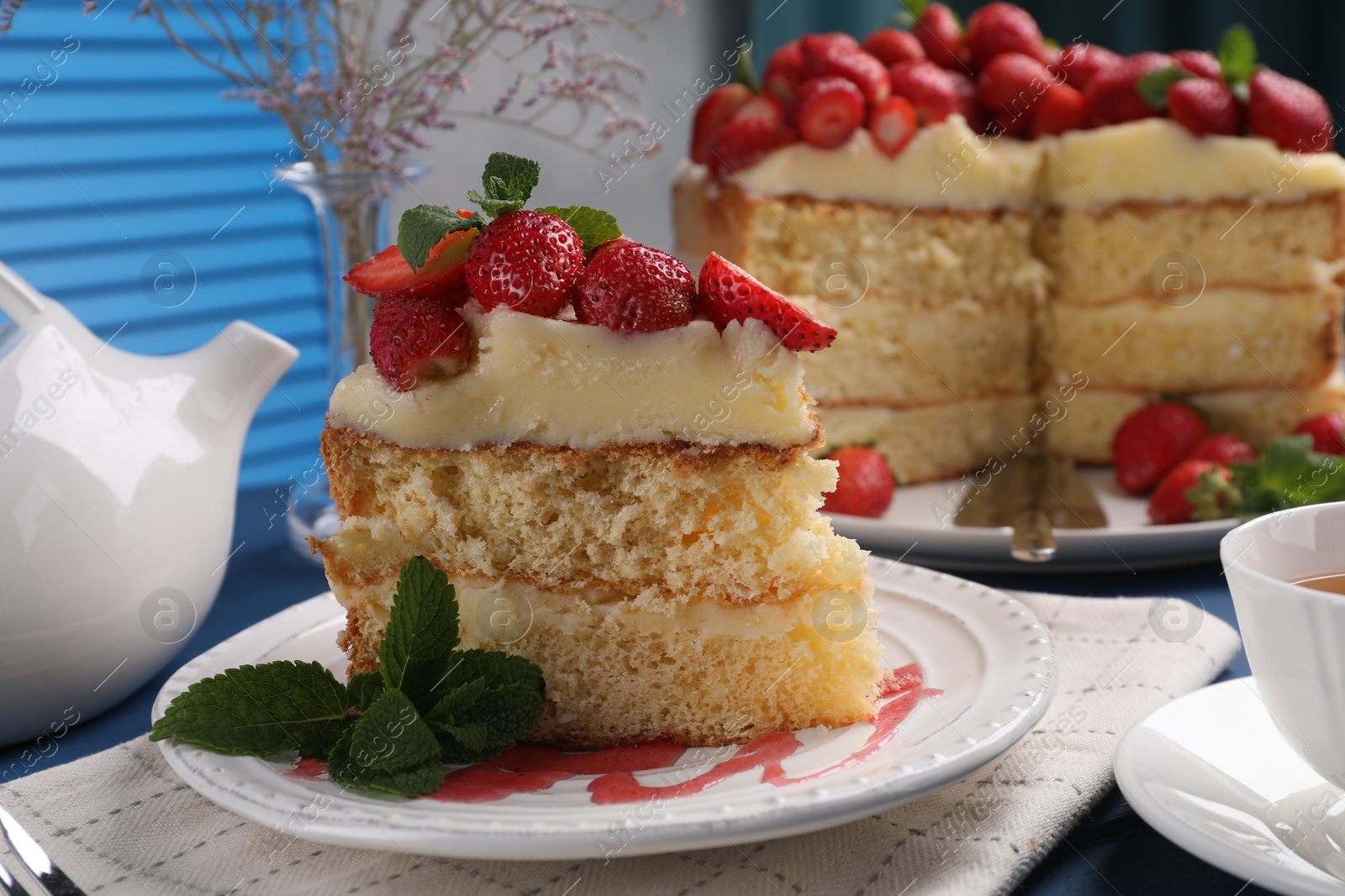 Photo of Piece of tasty cake with fresh strawberries, mint and cup of tea on table, closeup