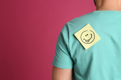 Photo of Man with smiling face sticker on back against pink background, space for text. April fool's day