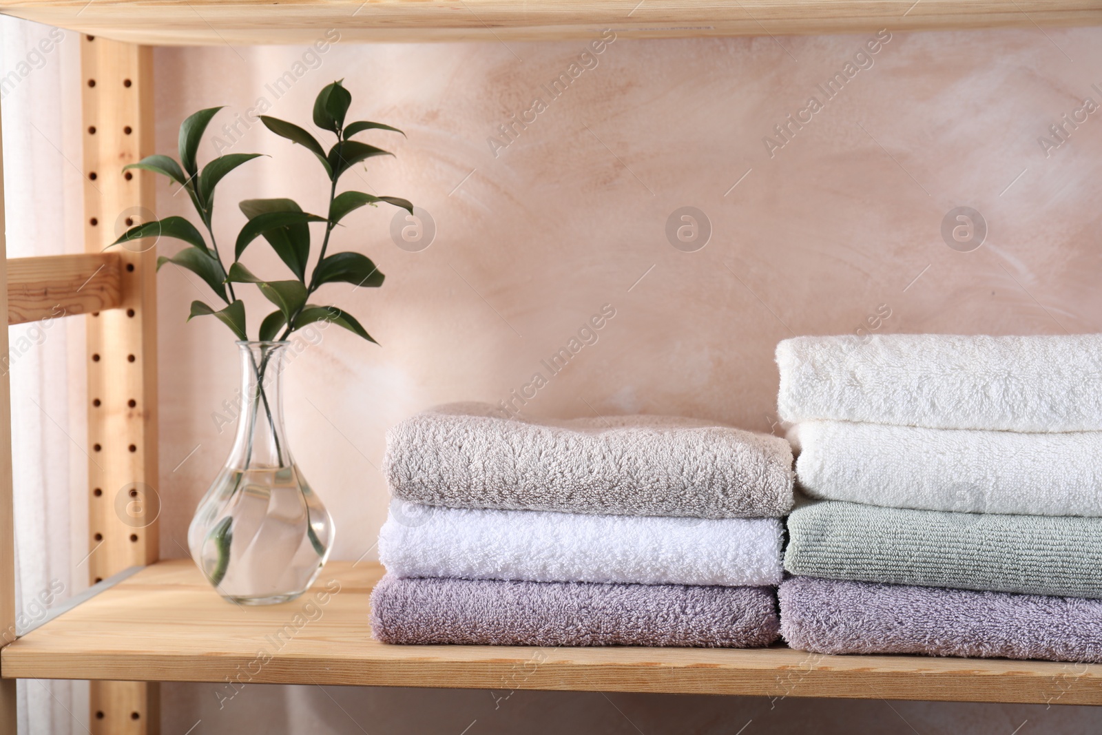 Photo of Stacked soft towels and green leaves on wooden shelf indoors