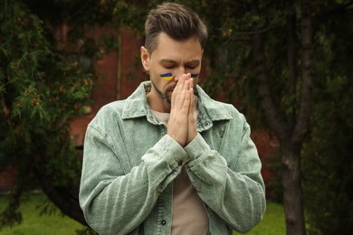 Photo of Sad man with drawings of Ukrainian flag on face outdoors