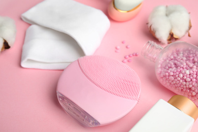 Face cleansing brush and cosmetic products on pink background