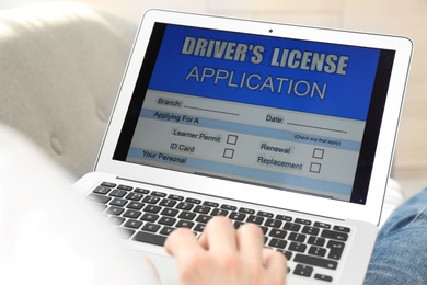 Photo of Man using laptop to fill driver's license application form at home, closeup