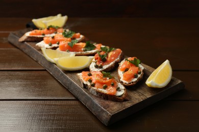 Photo of Tasty canapes with salmon, capers, lemon and cream cheese on wooden table