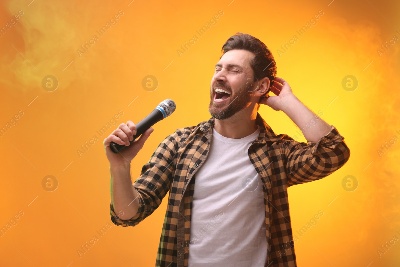 Photo of Handsome man with microphone singing on golden background