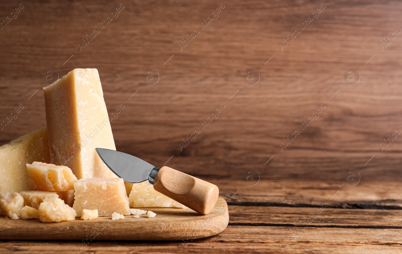 Photo of Pieces of delicious parmesan cheese with knife on wooden table. Space for text