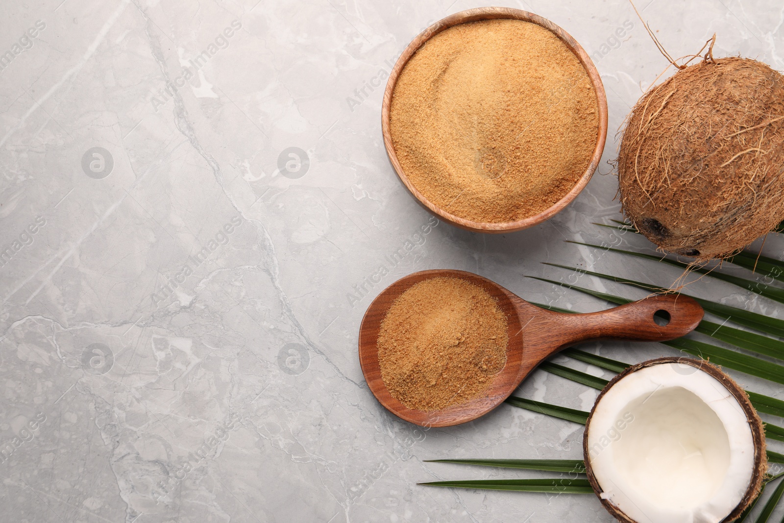 Photo of Spoon with coconut sugar, palm leaves, bowl and fruit on grey marble table, flat lay. Space for text