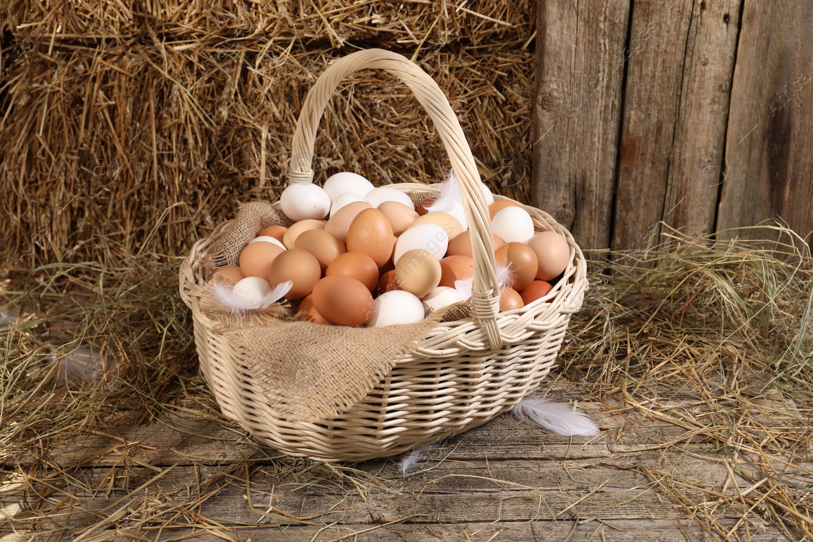 Photo of Wicker basket with fresh chicken eggs and dried straw in henhouse