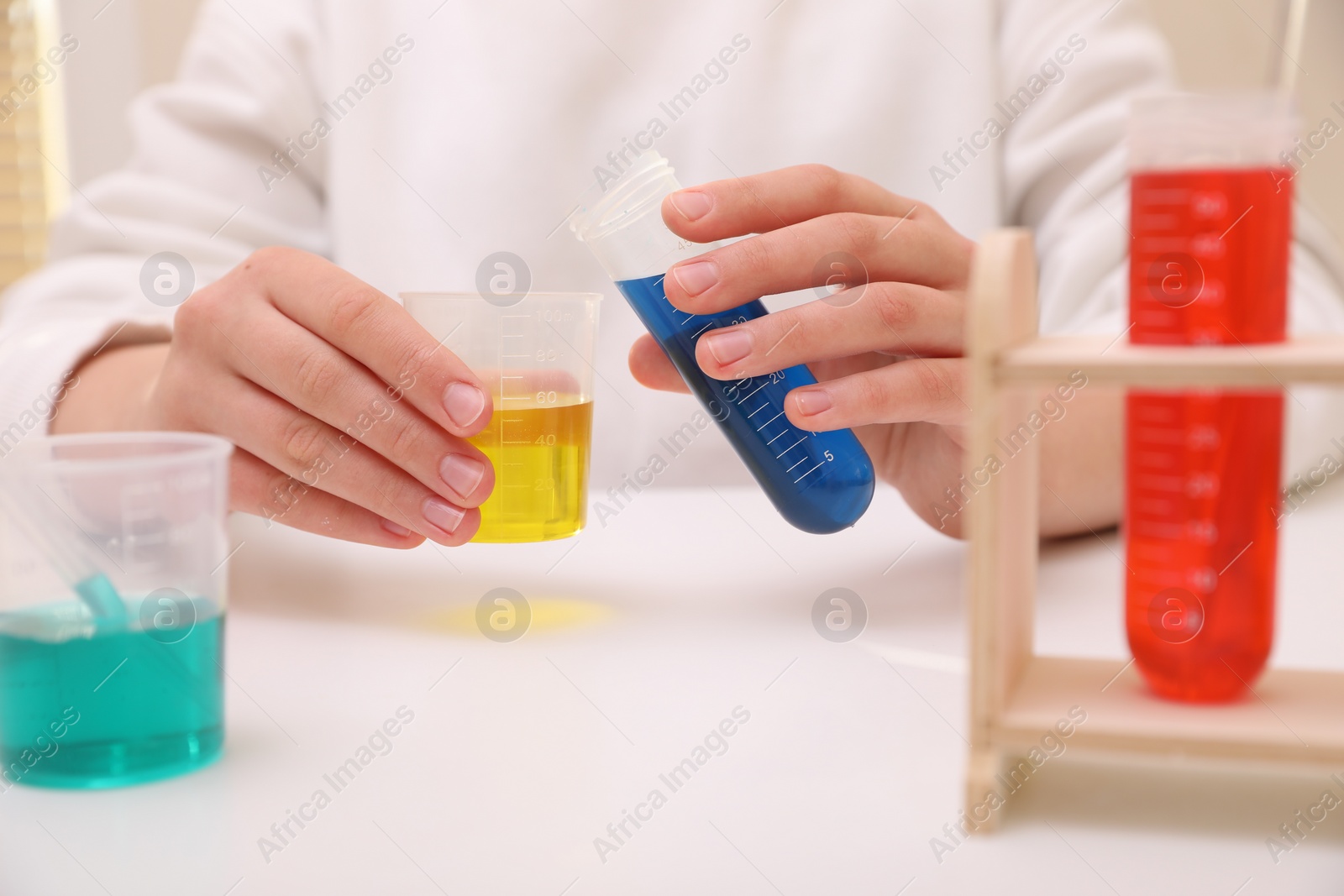 Photo of Girl mixing colorful liquids at white table indoors, closeup. Chemical experiment set for kids