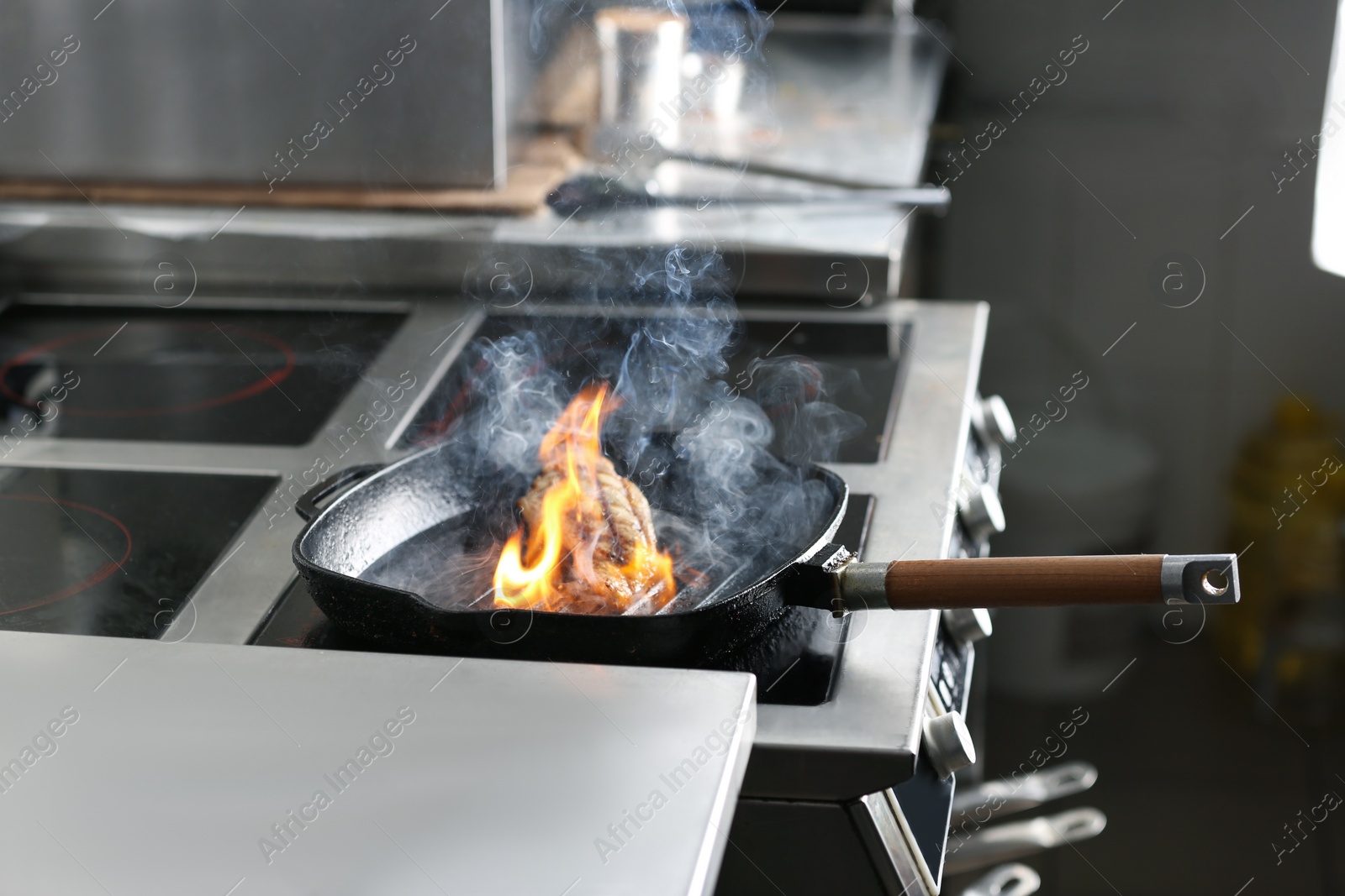 Photo of Cooking meat with burning flame in restaurant kitchen