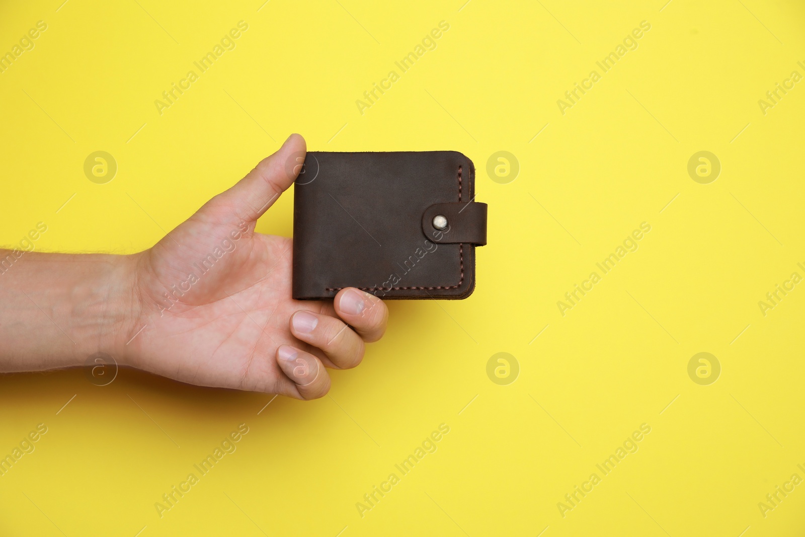 Photo of Man holding leather wallet on yellow background, closeup. Space for text