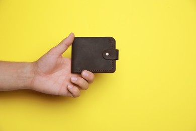 Photo of Man holding leather wallet on yellow background, closeup. Space for text