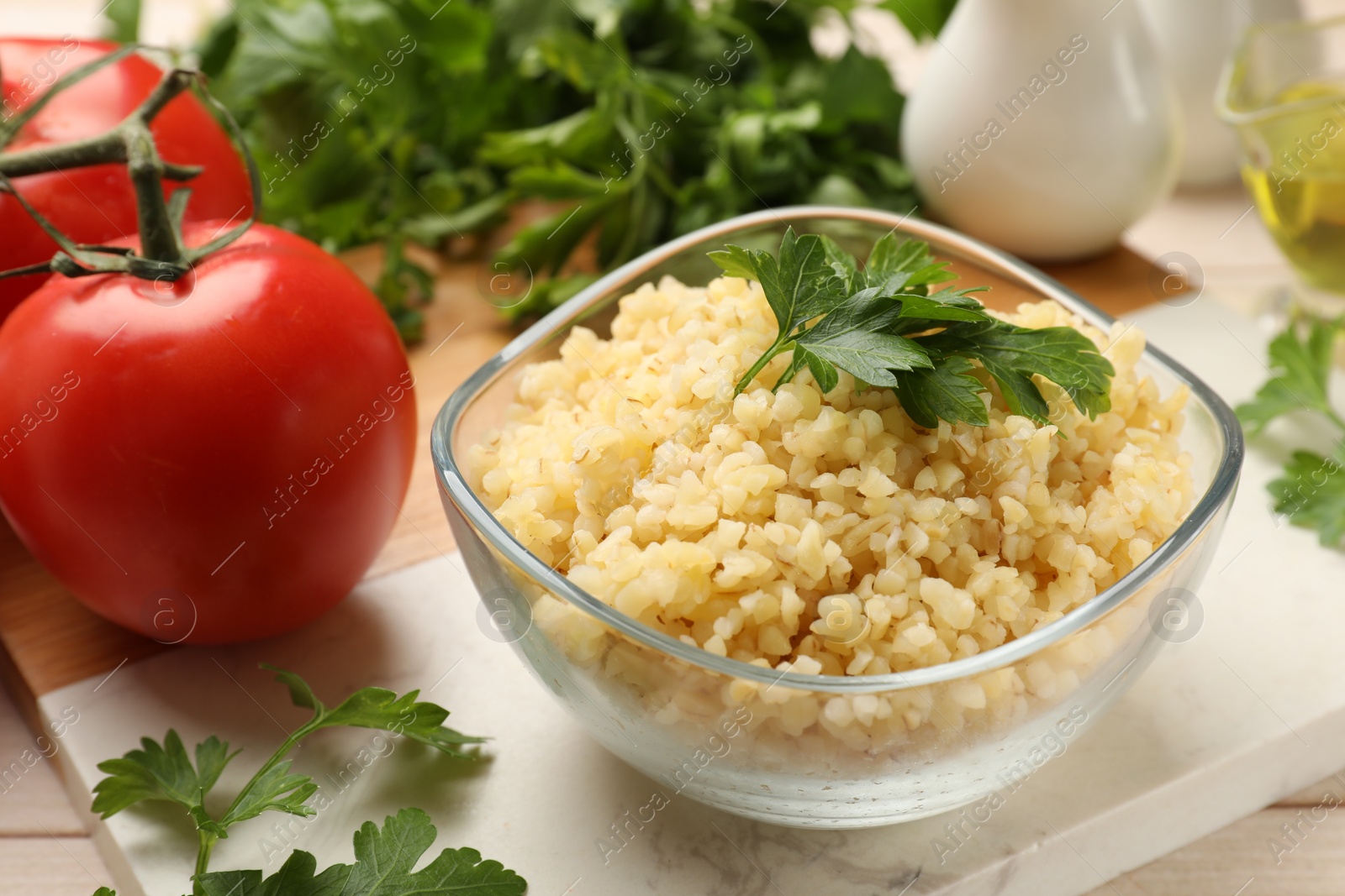 Photo of Delicious bulgur with parsley in bowl and tomatoes on table, closeup