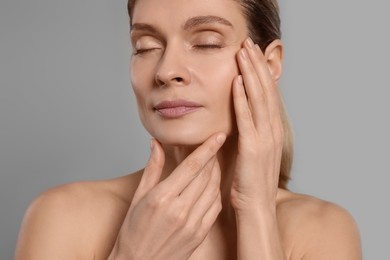 Woman massaging her face on grey background