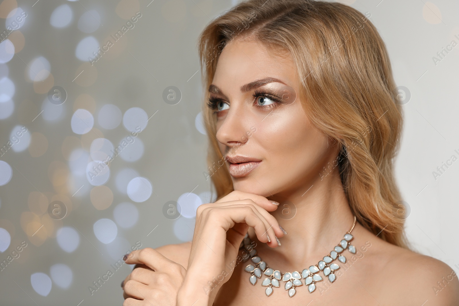 Photo of Beautiful young woman with elegant jewelry against defocused lights. Space for text