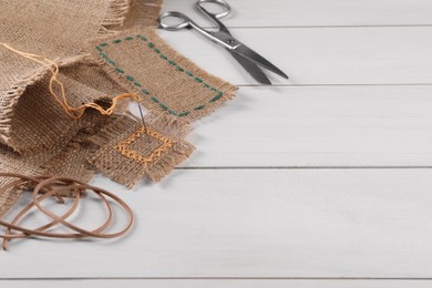 Pieces of burlap fabric with stitches, needle and scissors on white wooden table. Space for text