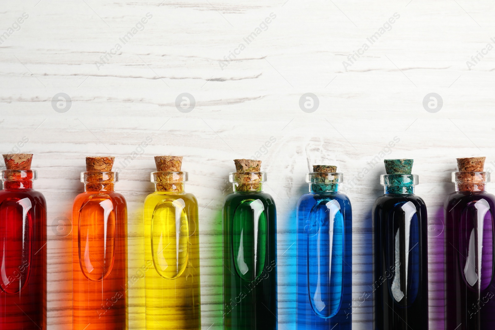 Photo of Glass bottles with different food coloring on white wooden table, flat lay. Space for text