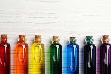 Photo of Glass bottles with different food coloring on white wooden table, flat lay. Space for text