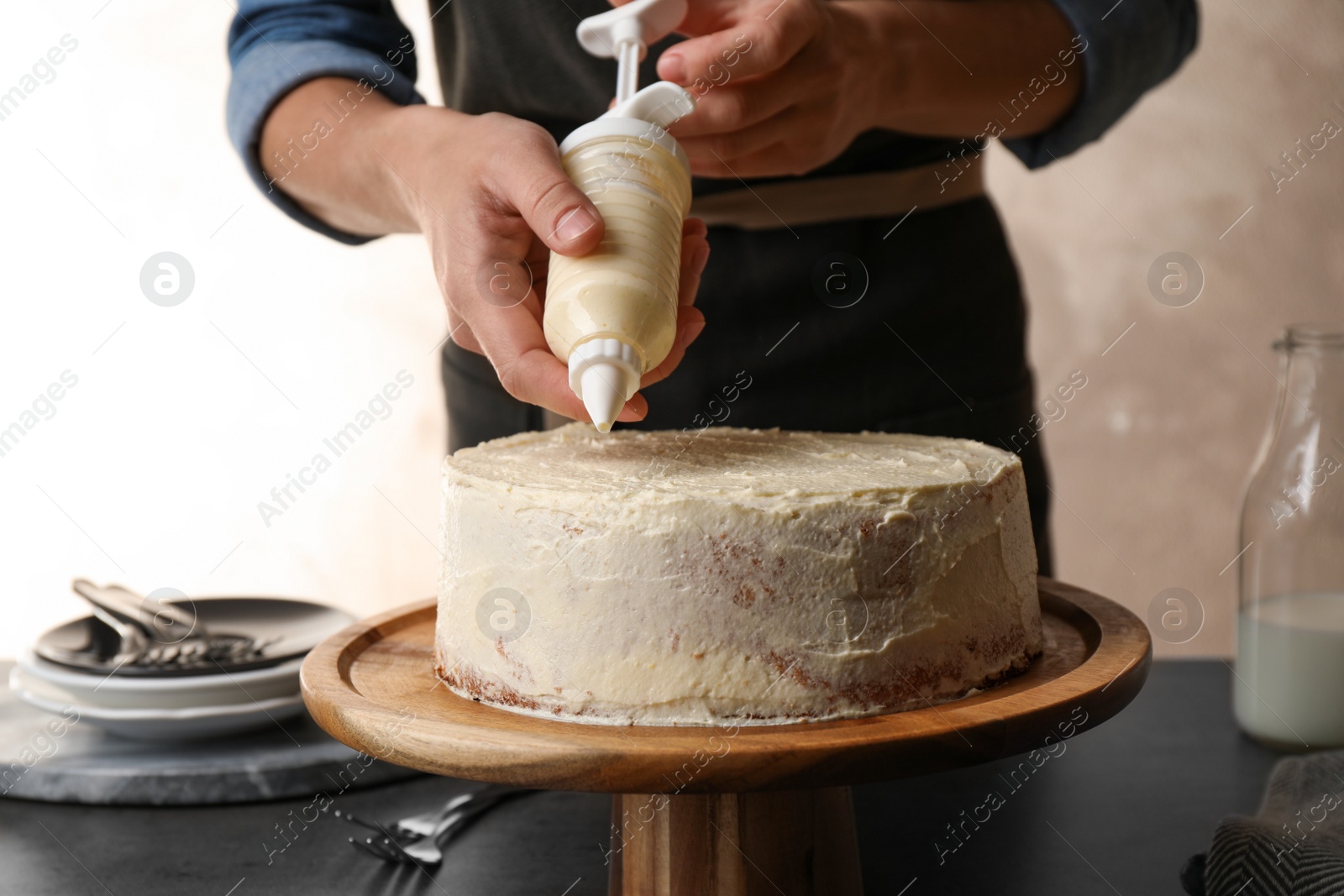 Photo of Woman decorating delicious cake with fresh cream at table indoors, closeup. Homemade pastry