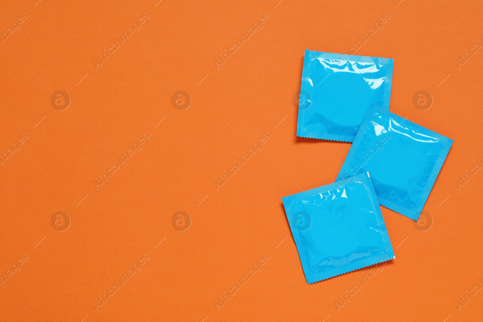 Photo of Condom packages on orange background, flat lay and space for text. Safe sex