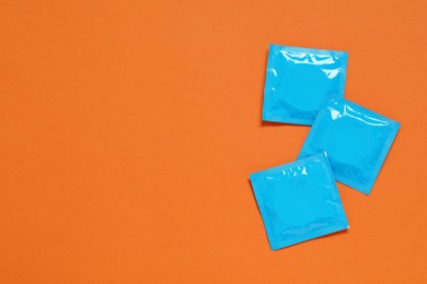 Photo of Condom packages on orange background, flat lay and space for text. Safe sex