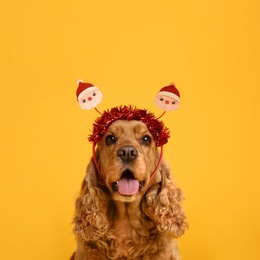 Adorable Cocker Spaniel dog in Santa headband on yellow background