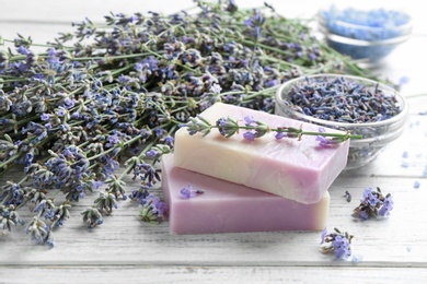 Photo of Handmade soap bars with lavender flowers on white wooden table. Space for text