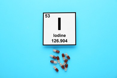 Photo of Card with iodine element and pills on light blue background, flat lay