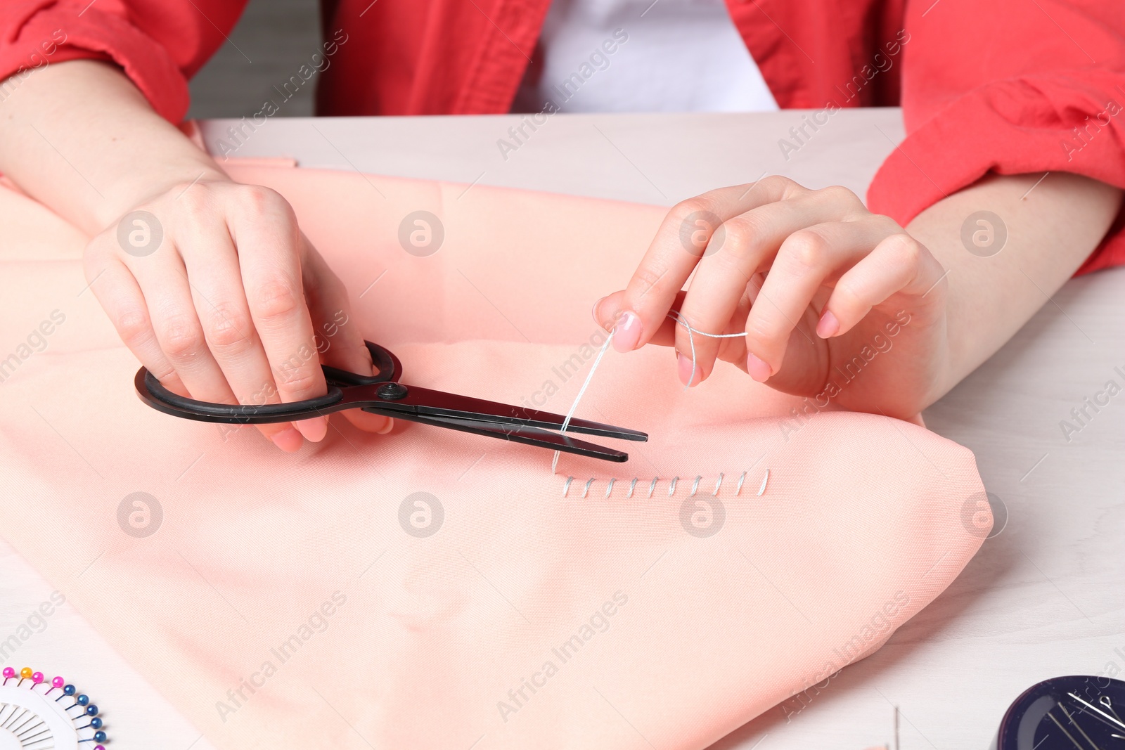 Photo of Woman cutting sewing thread over cloth at white wooden table, closeup