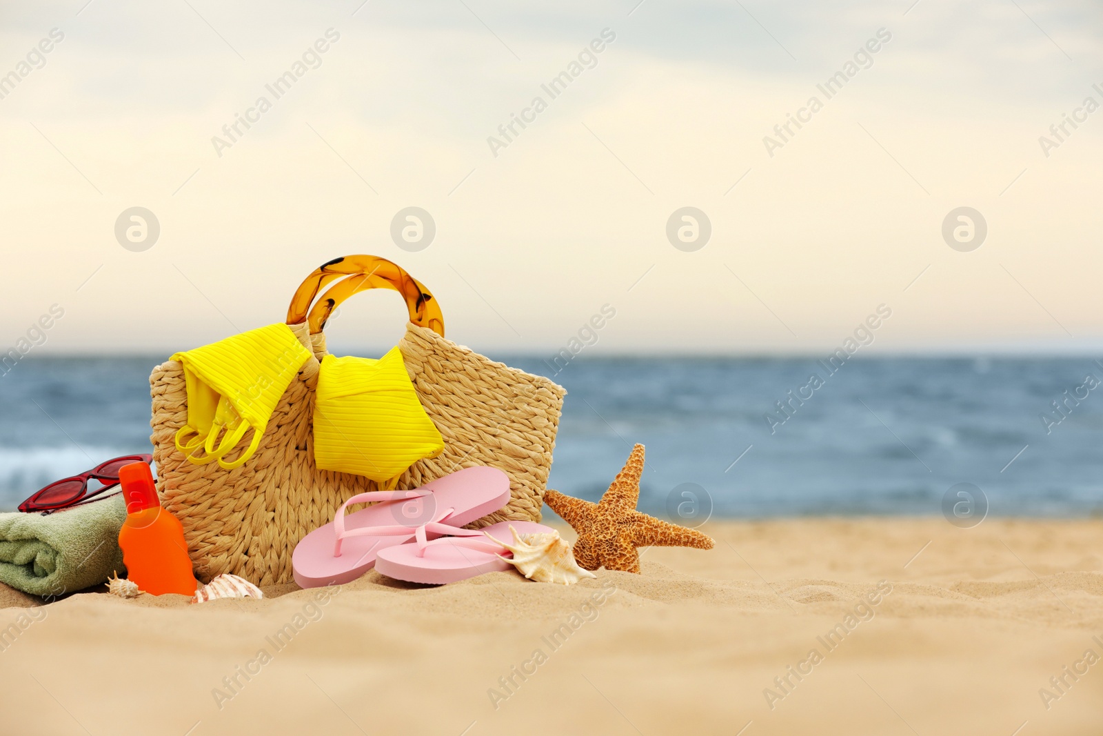 Photo of Bag and different beach objects on sand near sea, space for text