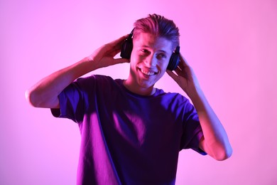 Photo of Young man with headphones on pink background in neon lights