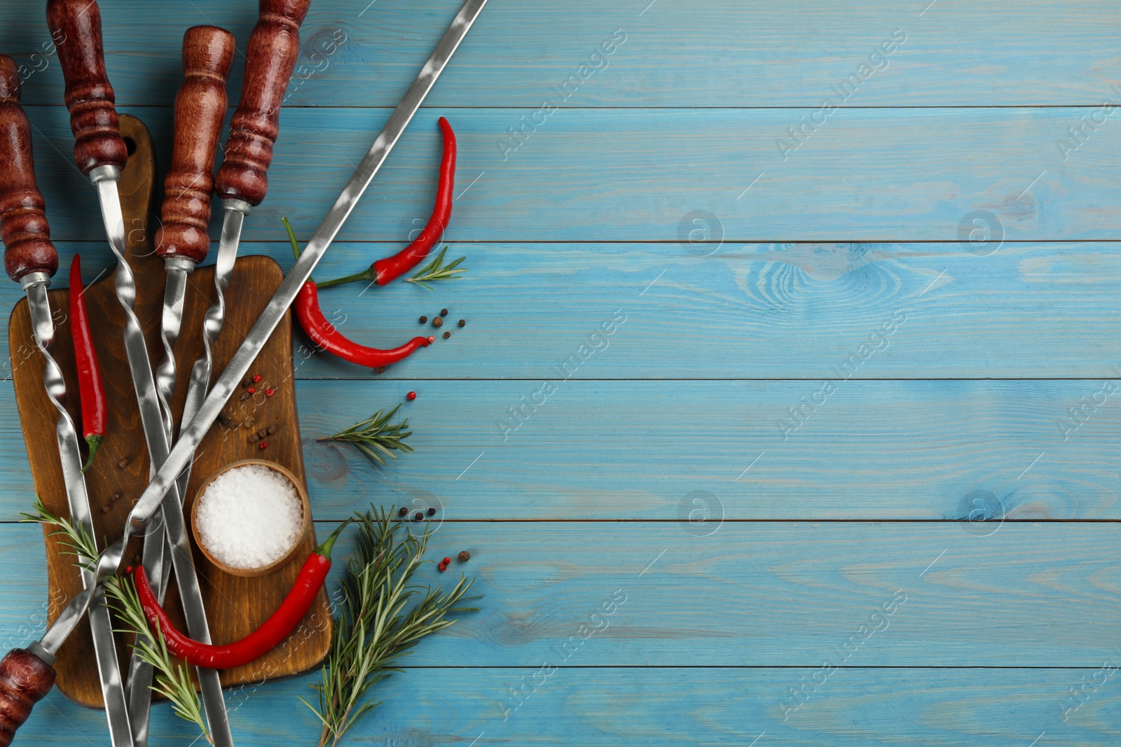 Photo of Flat lay composition with metal skewers on light blue wooden table. Space for text