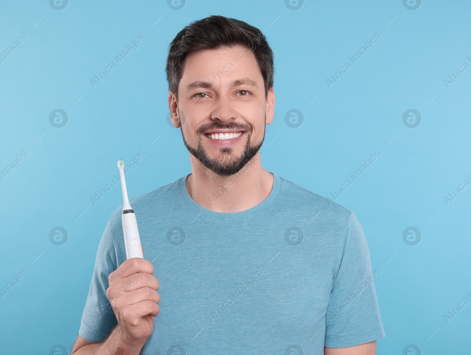 Photo of Happy man holding electric toothbrush on light blue background