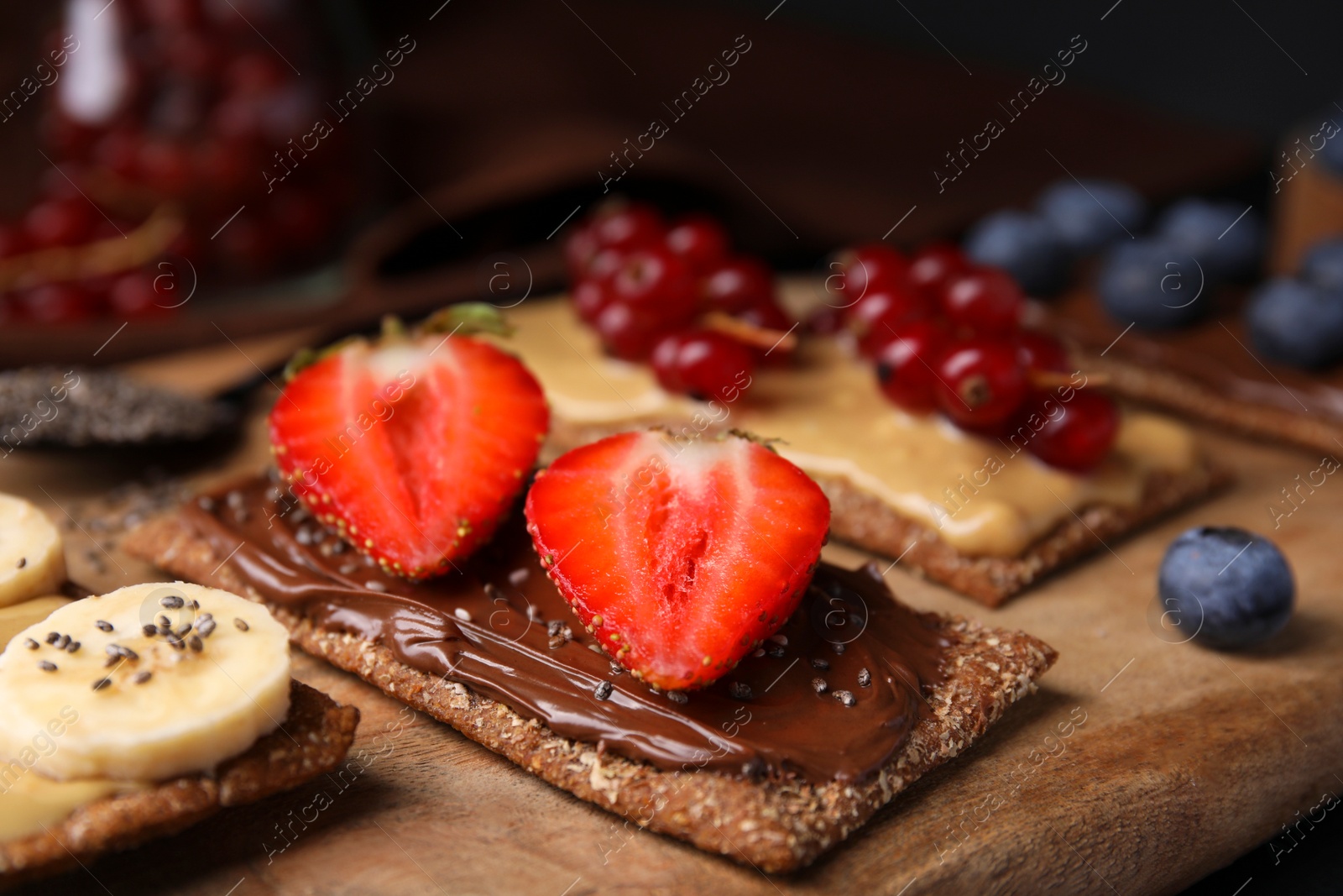 Photo of Fresh crunchy rye crispbreads with different toppings on wooden board, closeup