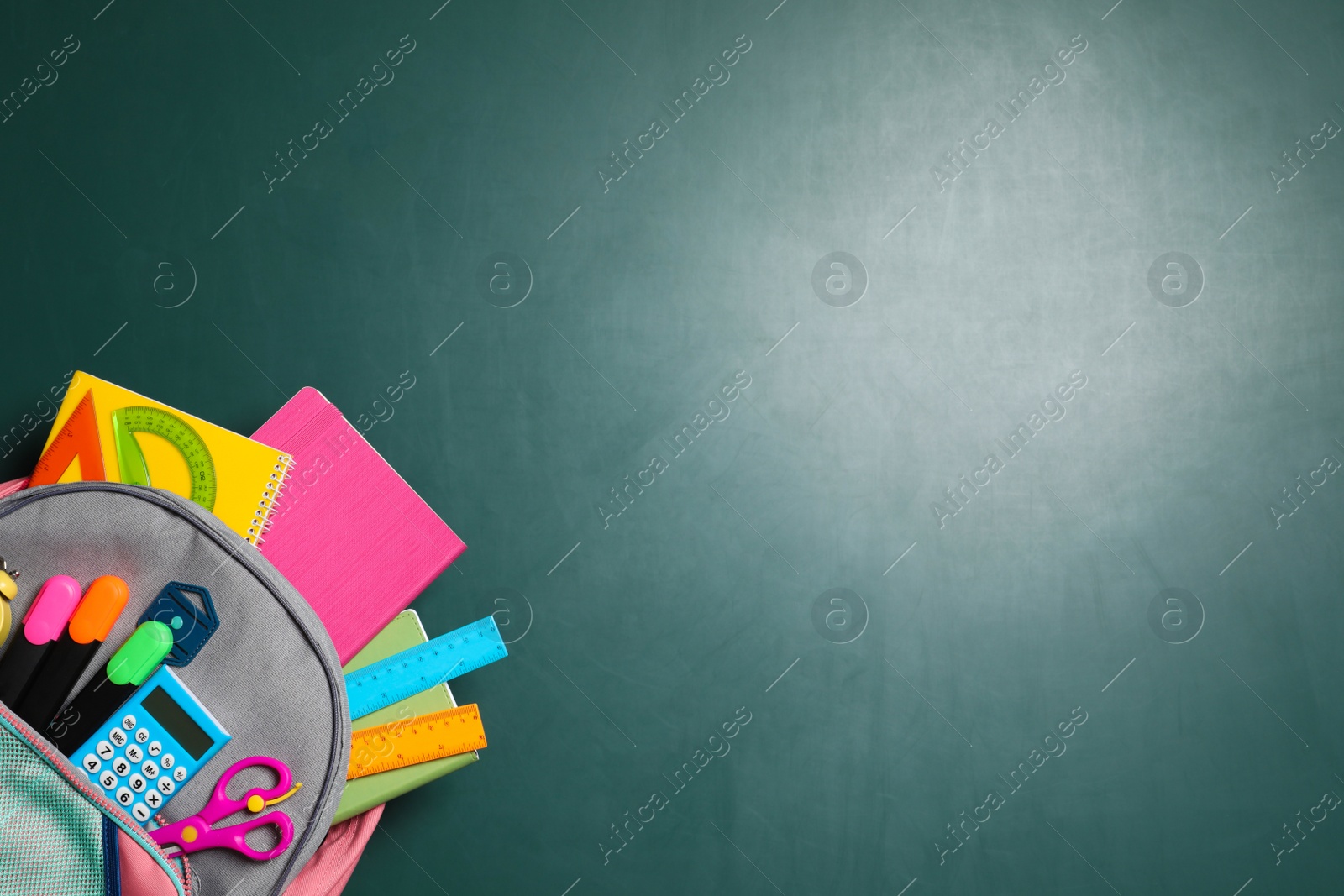 Photo of Backpack with different stationery on chalkboard background, top view. Space for text