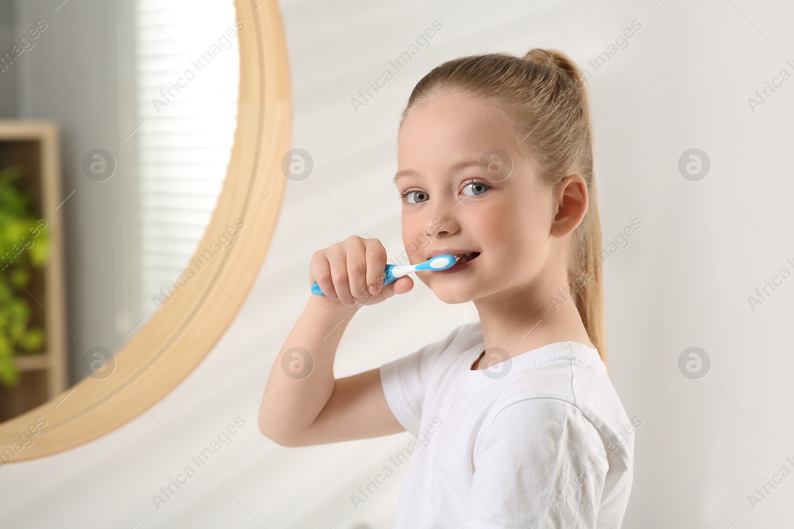 Photo of Cute little girl brushing her teeth with plastic toothbrush in bathroom, space for text