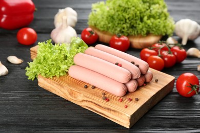 Photo of Fresh raw vegetarian sausages with pepper and vegetables on black wooden table