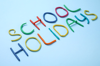 Photo of Phrase School Holidays made of modeling clay on light blue background