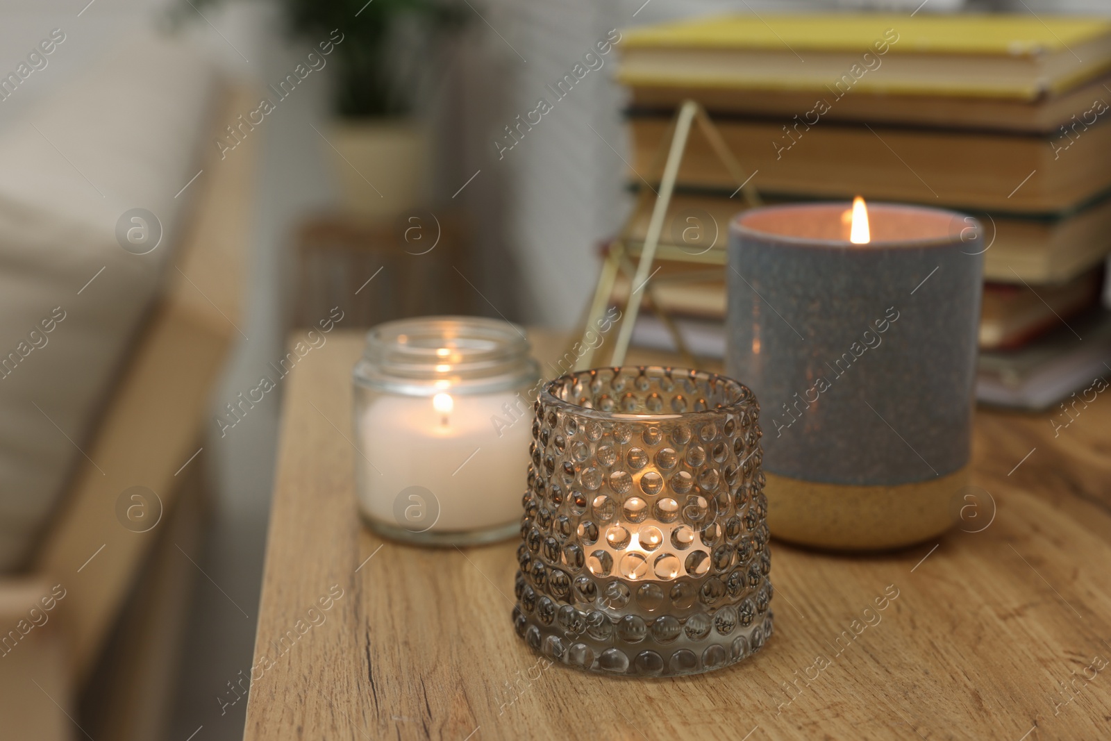 Photo of Lit candles in different holders on wooden table indoors. Space for text