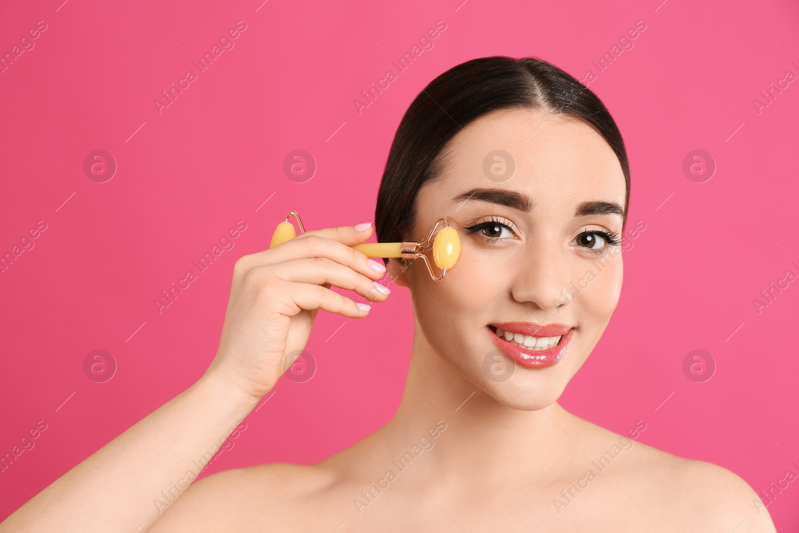 Photo of Woman using natural jade face roller on pink background