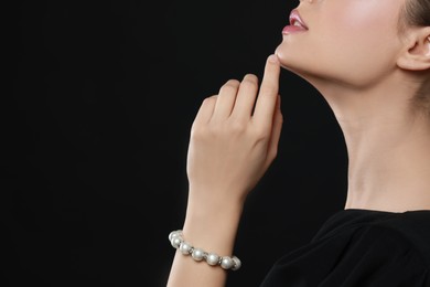 Photo of Young woman wearing elegant pearl bracelet on black background, closeup. Space for text