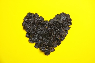 Photo of Heart shaped heap of tasty prunes on color background, top view. Dried fruit as healthy snack