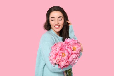 Beautiful young woman with bouquet of peonies on pink background